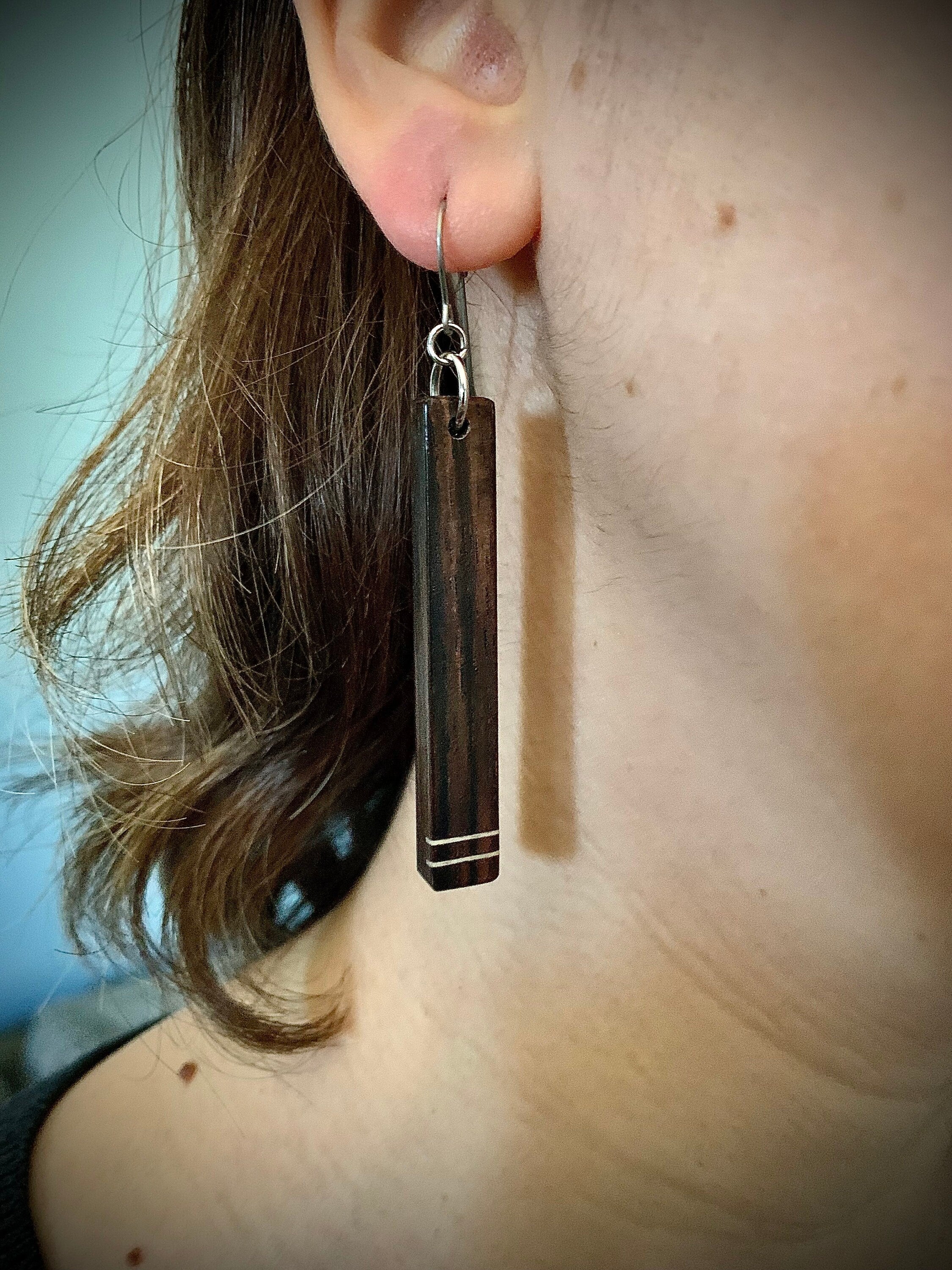 A dark wood dangle earring with two horizontal white stripes on a female model.