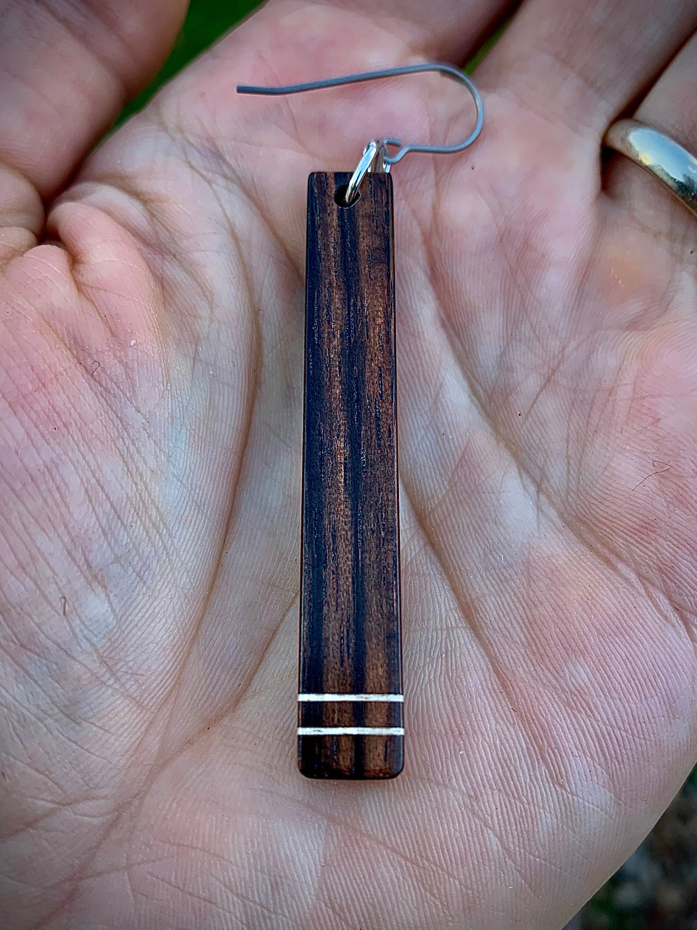 A dark wood dangle earring with two horizontal white stripes in the palm of a hand to show size.