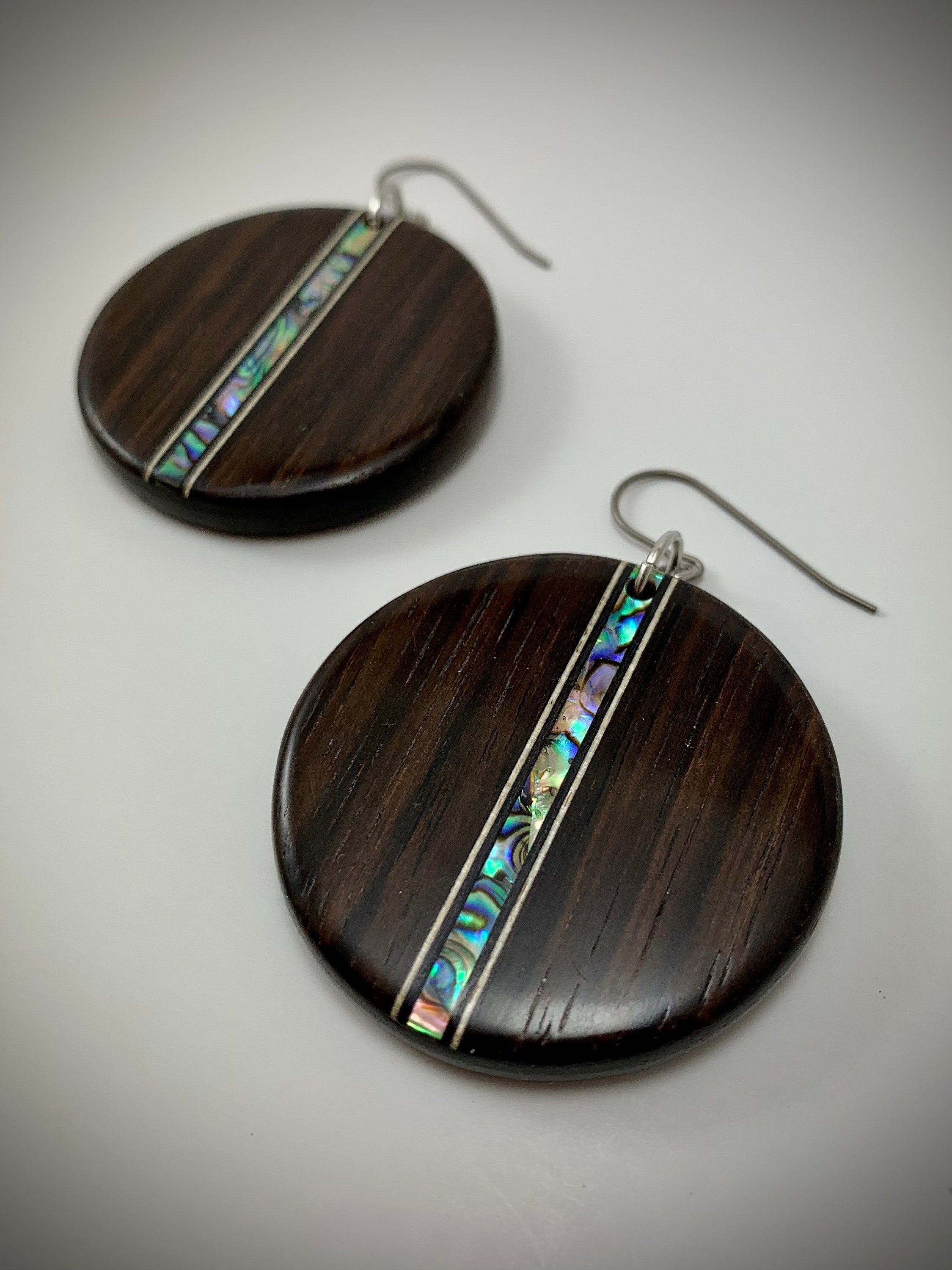 Two round dangle earrings made of dark wood with a shimmering shell inlay running down the center.