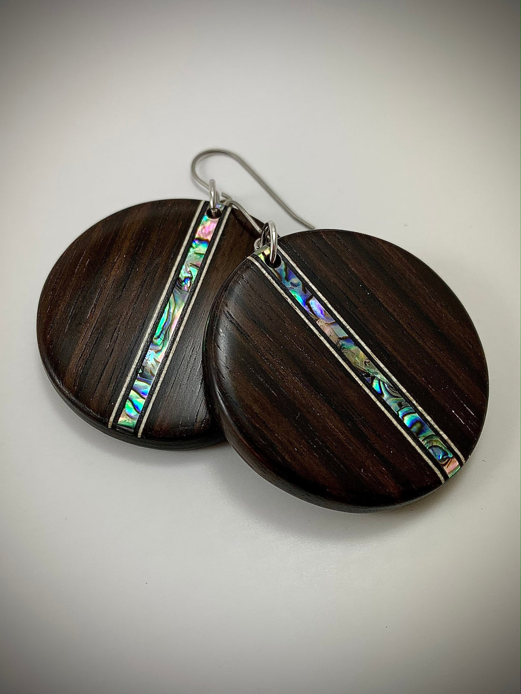 Two round dangle earrings made of dark wood with a shimmering shell inlay running down the center.