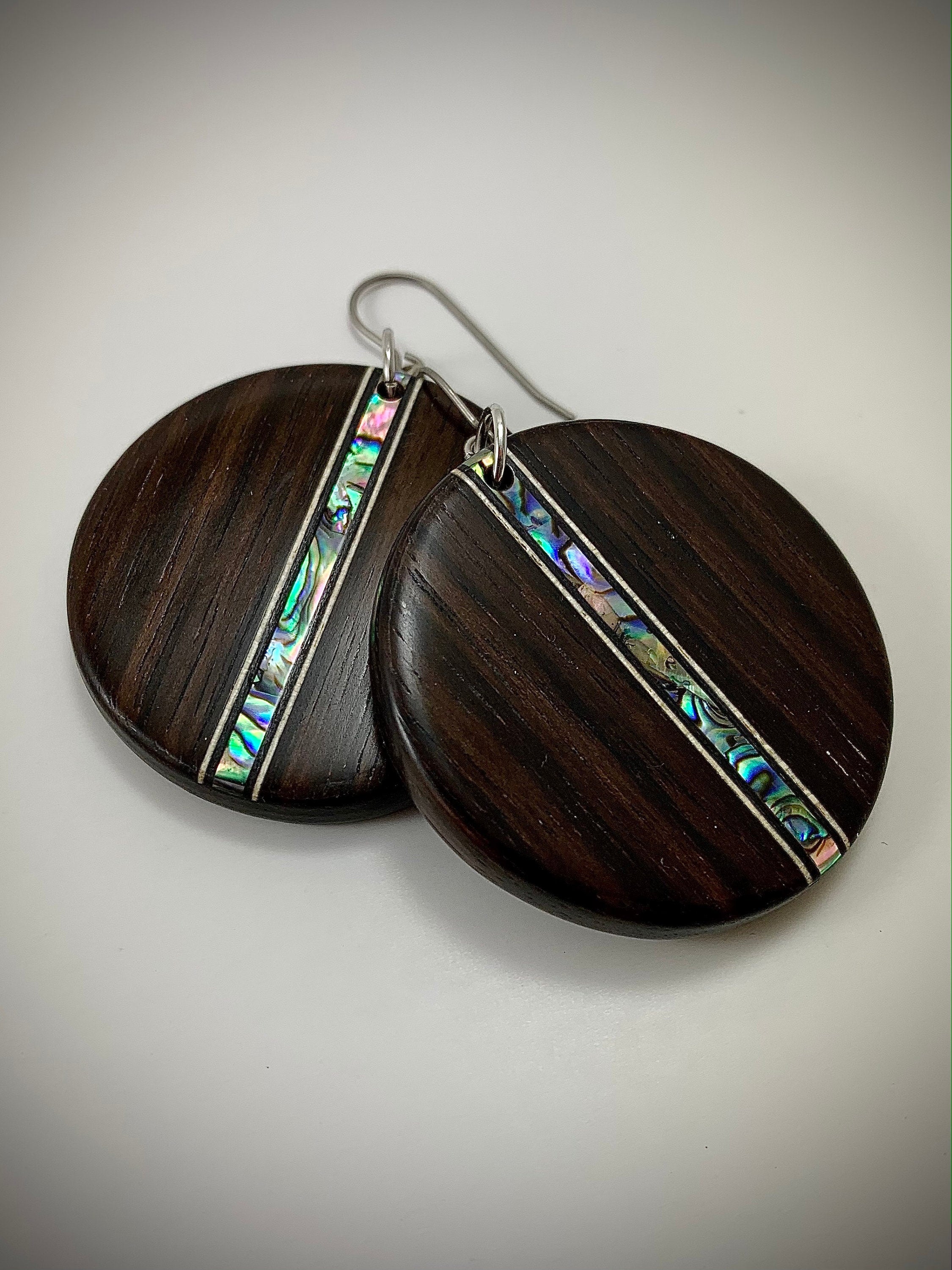 Two round dangle earrings made of dark wood with a shimmering shell inlay running down the center.