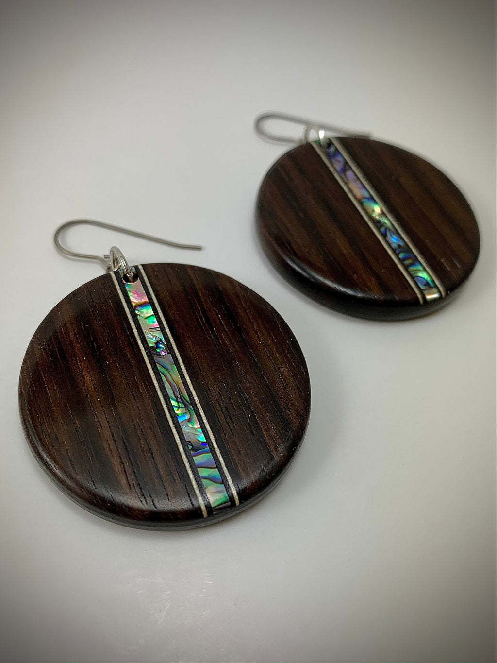 Two round dangle earrings made of dark wood with a shimmering shell inlay running down the center.
