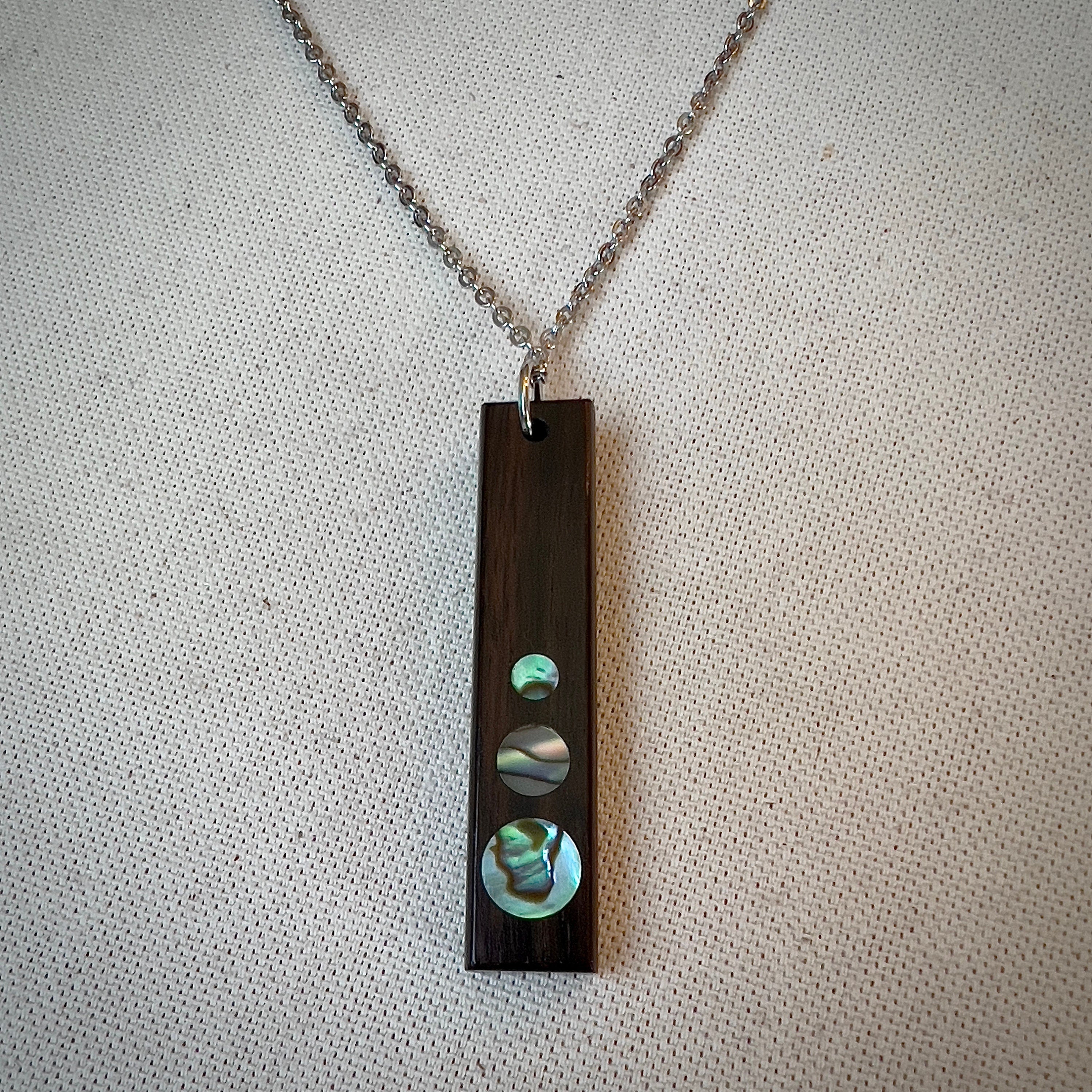 Rectangular wooden pendant with circular iridescent inlays on a silver chain.