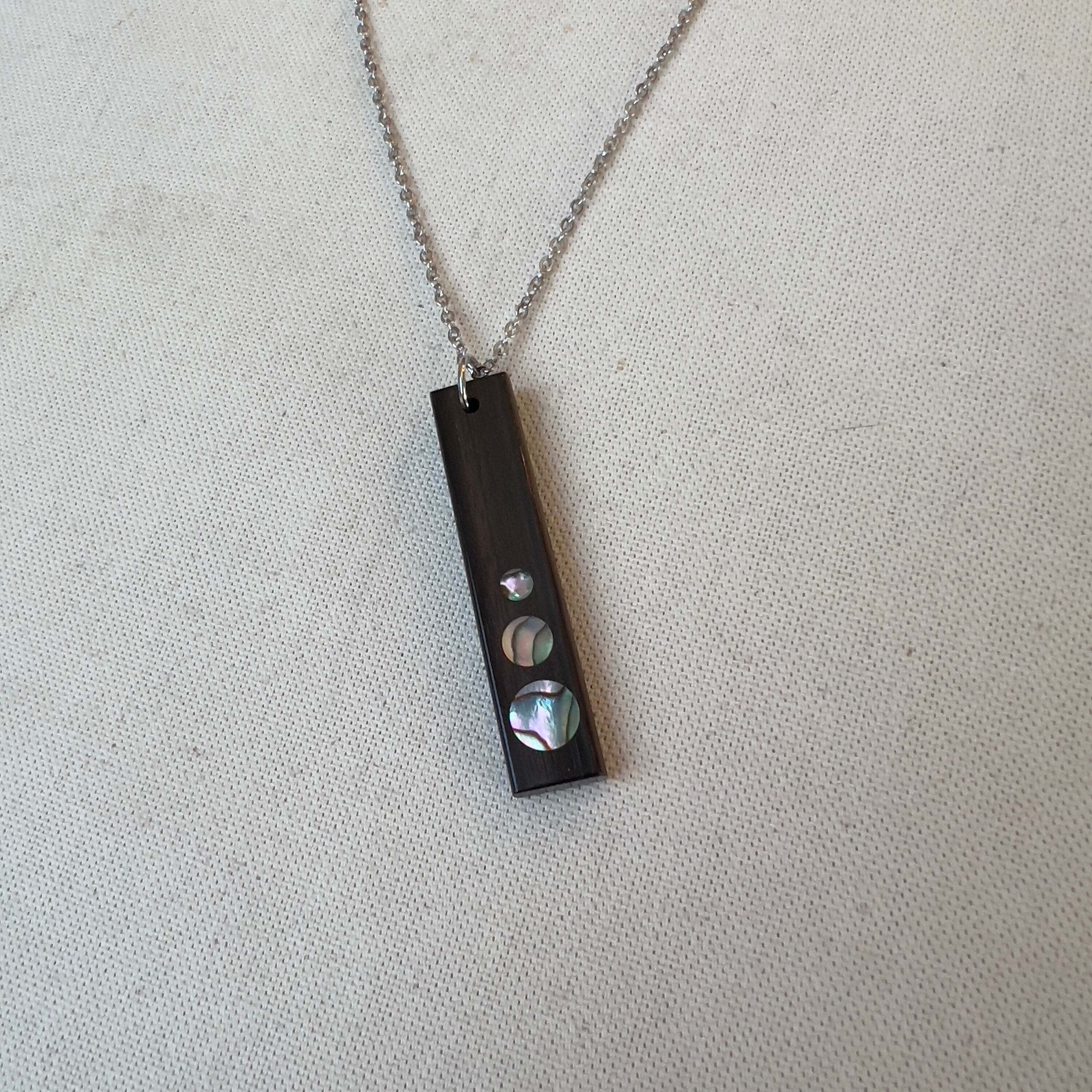 Rectangular wooden pendant with circular iridescent inlays on a silver chain.