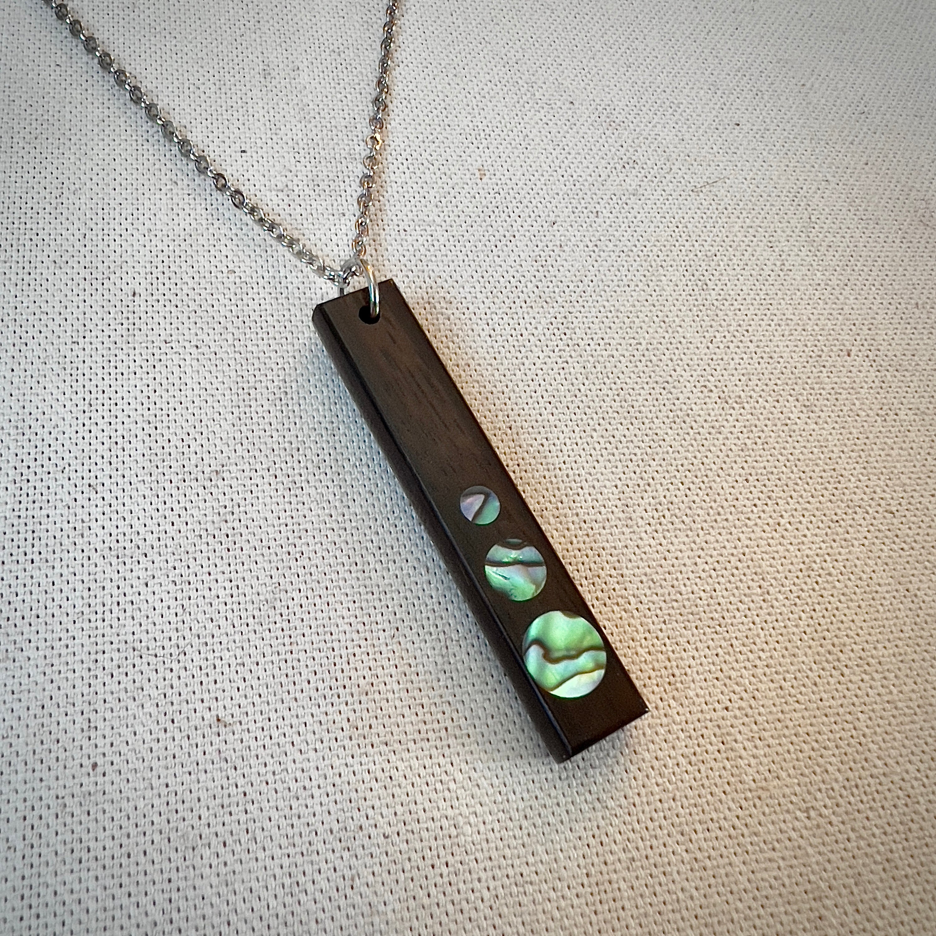 Rectangular wooden pendant with circular iridescent inlays on a silver chain.