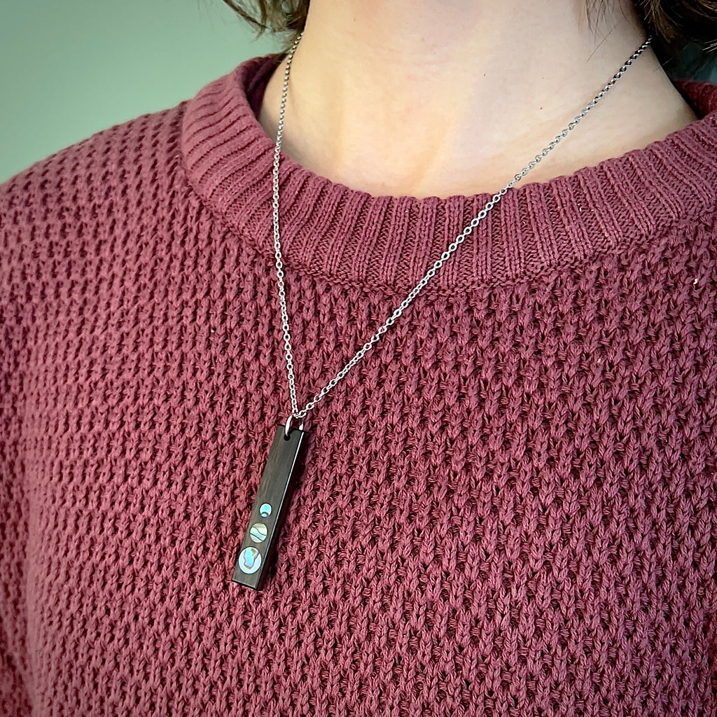 Close-up of a model wearing a knit sweater and a silver chain necklace with a rectangular pendant featuring three circular iridescent inlays.