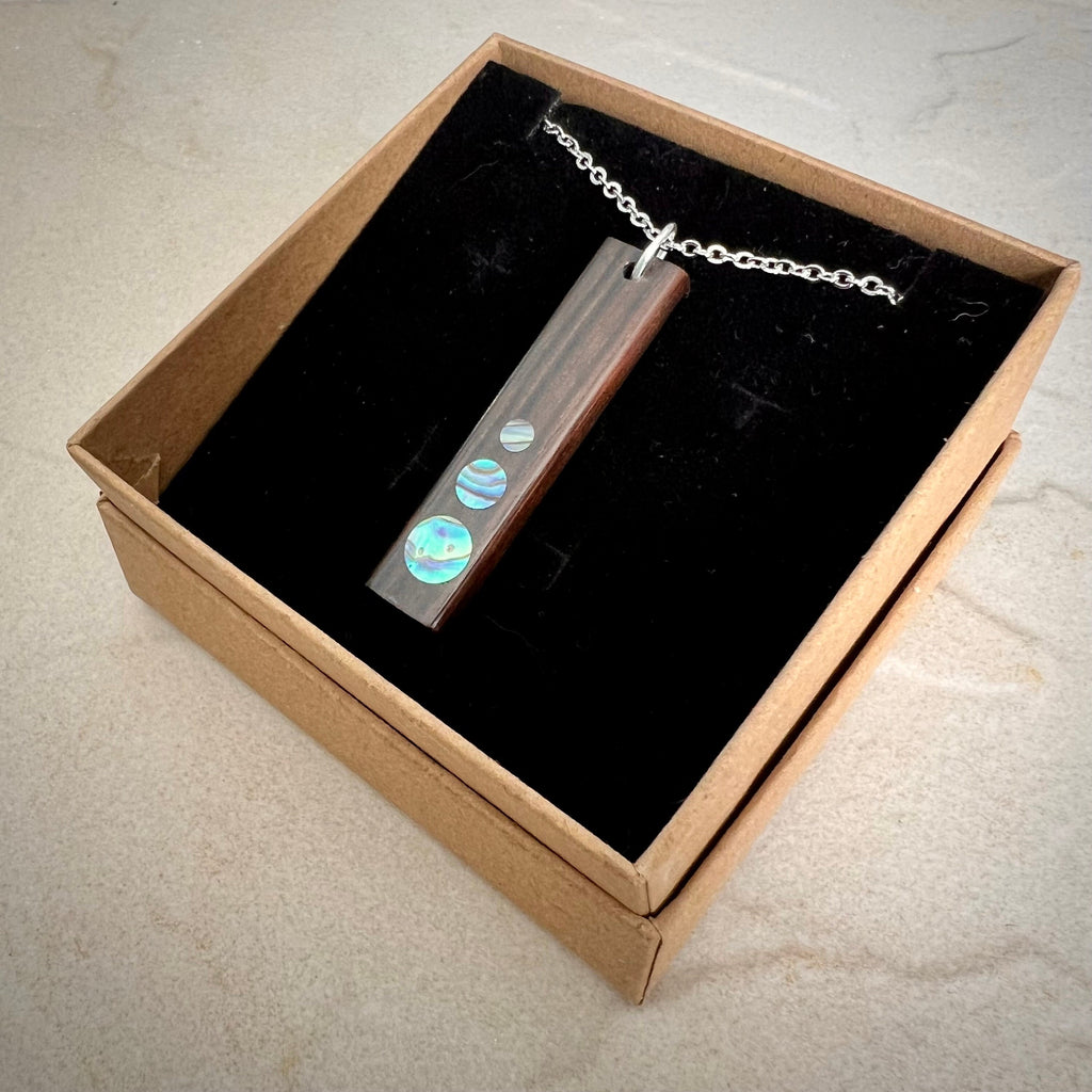 Rectangular pendant necklace with iridescent discs in a brown box with black lining.