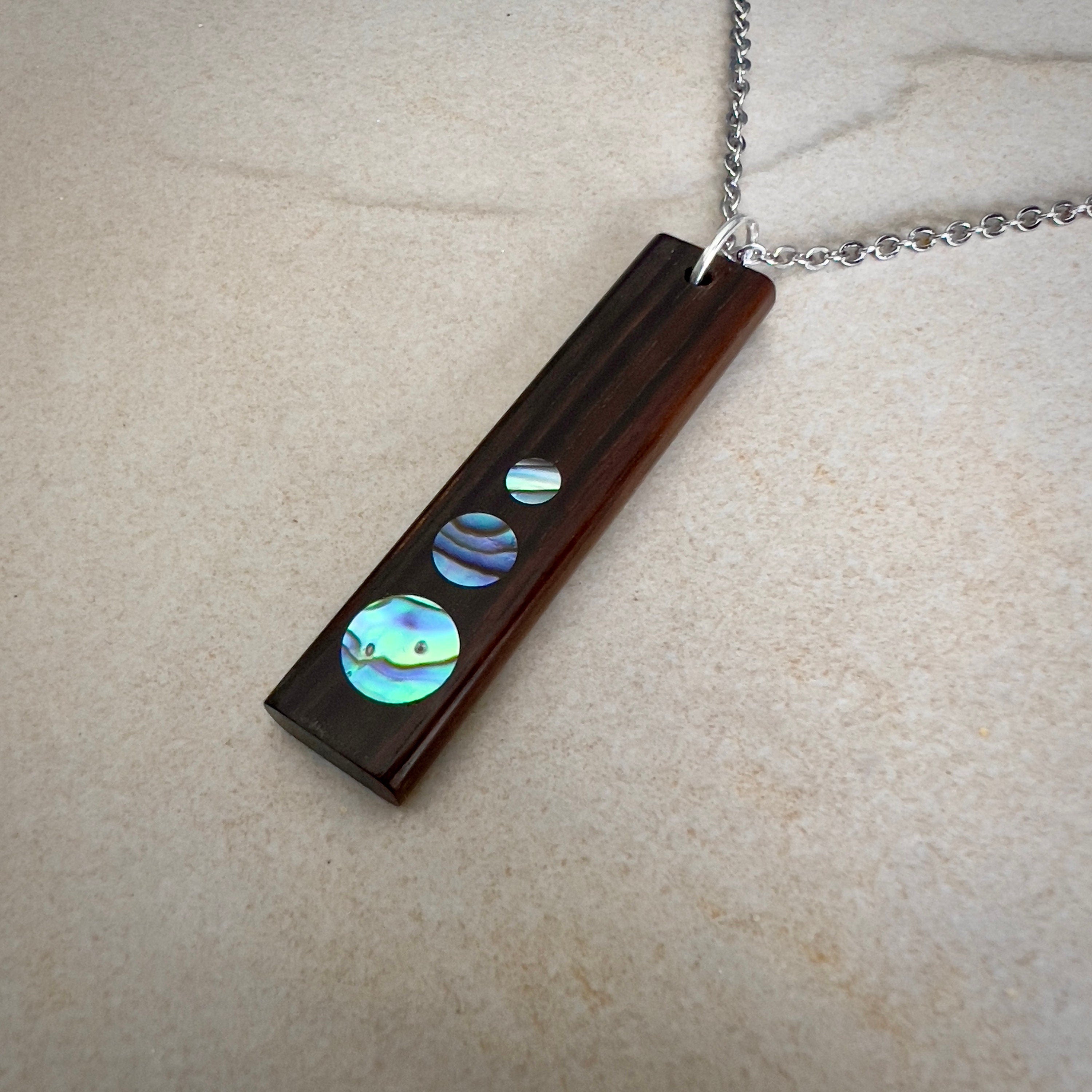 Rectangular wooden pendant with circular iridescent inlays on a silver chain.
