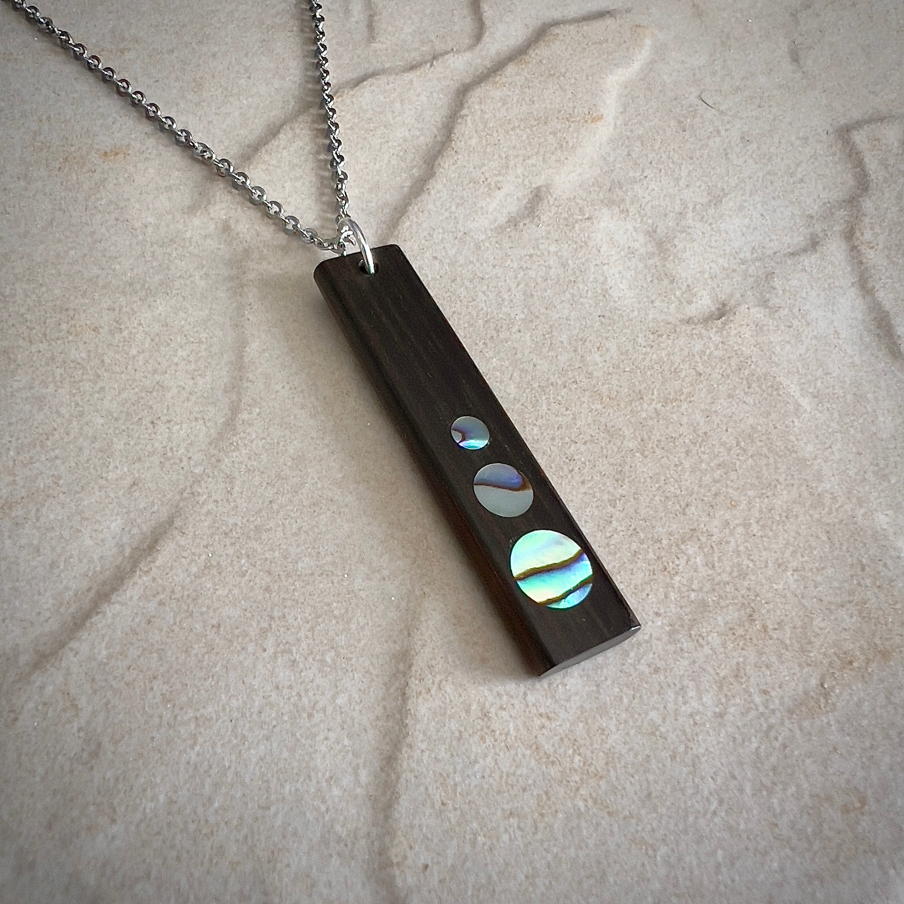 Rectangular wooden pendant with circular iridescent inlays on a silver chain.