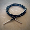 Coiled black braided rope with silver tips on a textured beige surface.