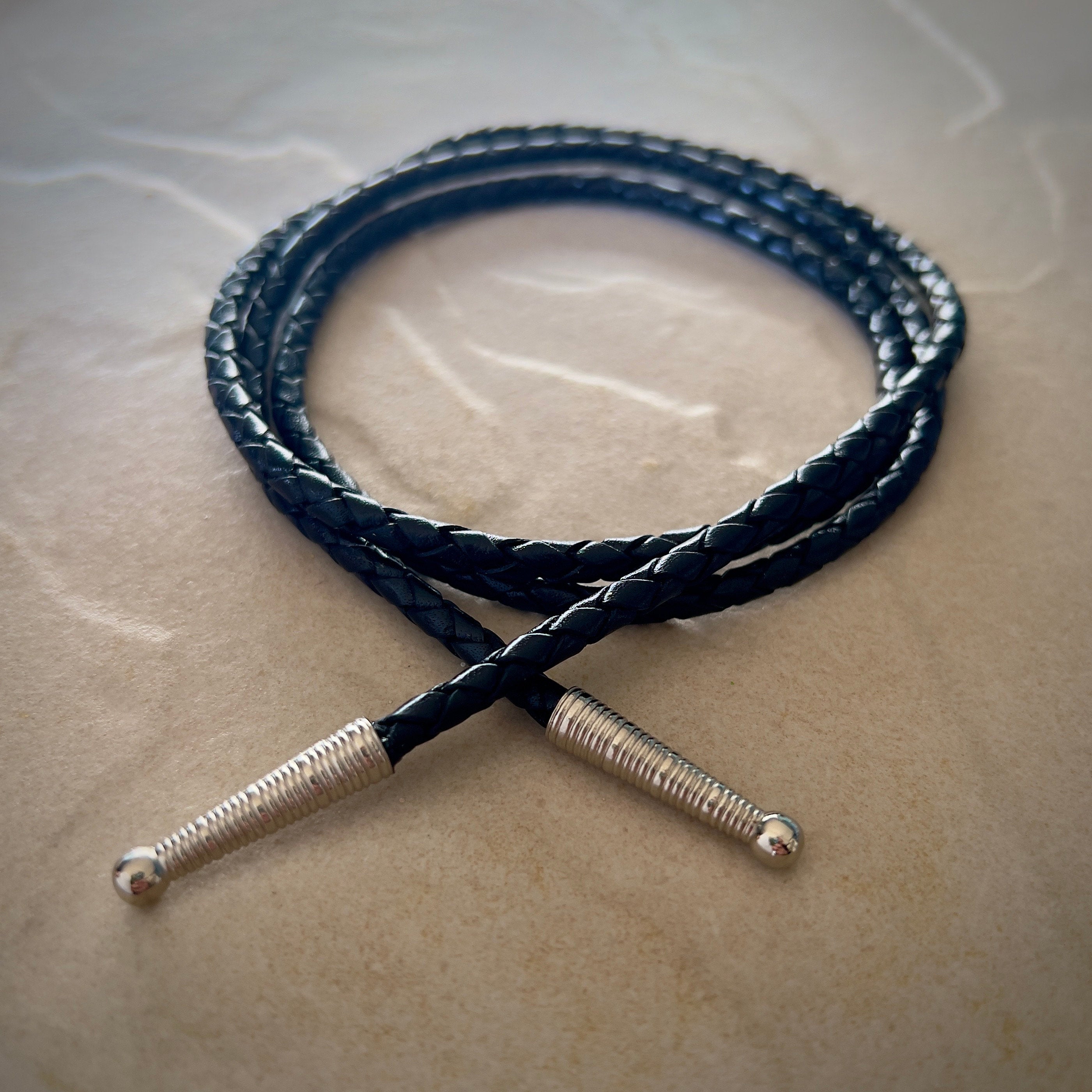 Coiled black braided rope with silver tips on a textured beige surface.