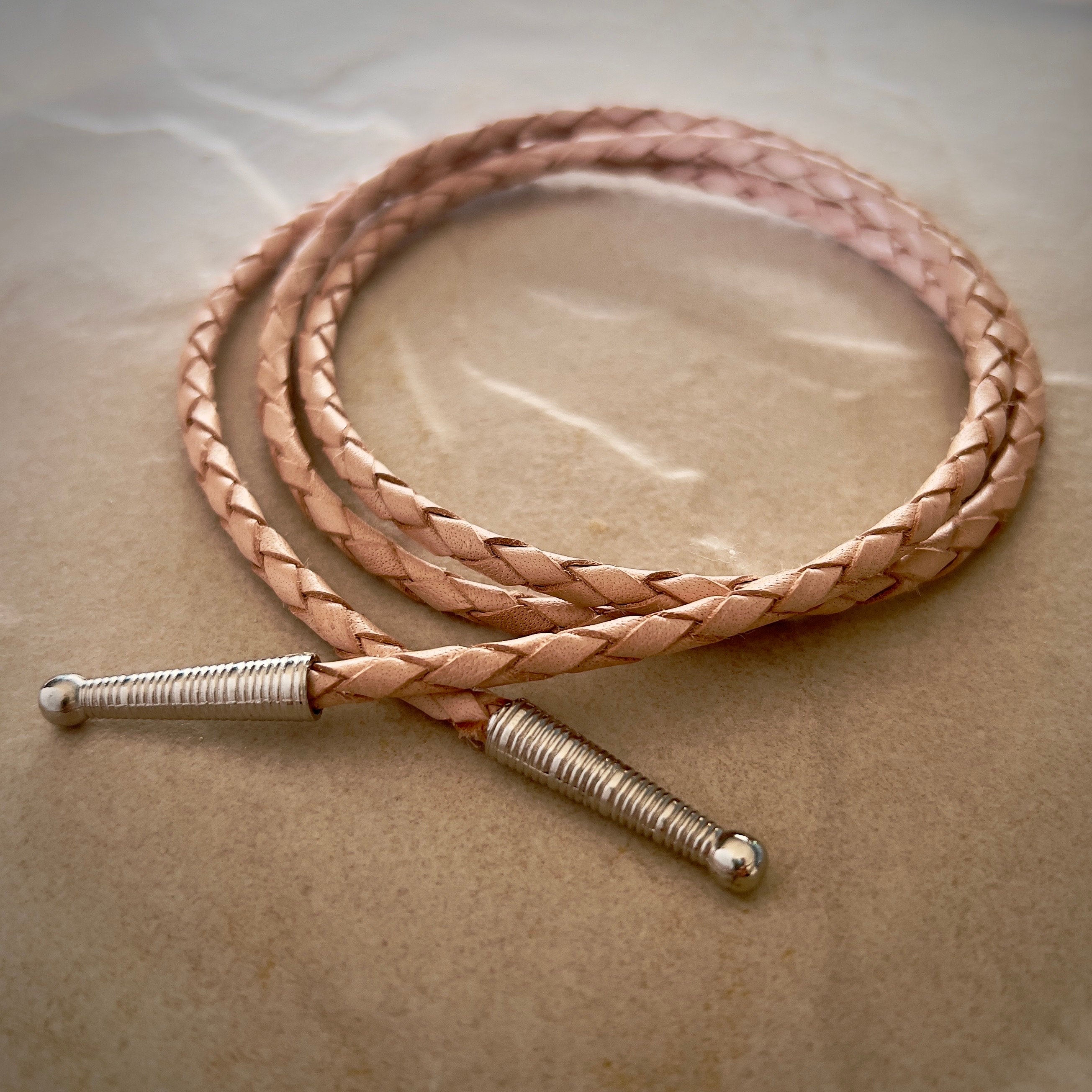 Coiled tan braided rope with silver tips on a textured beige surface.