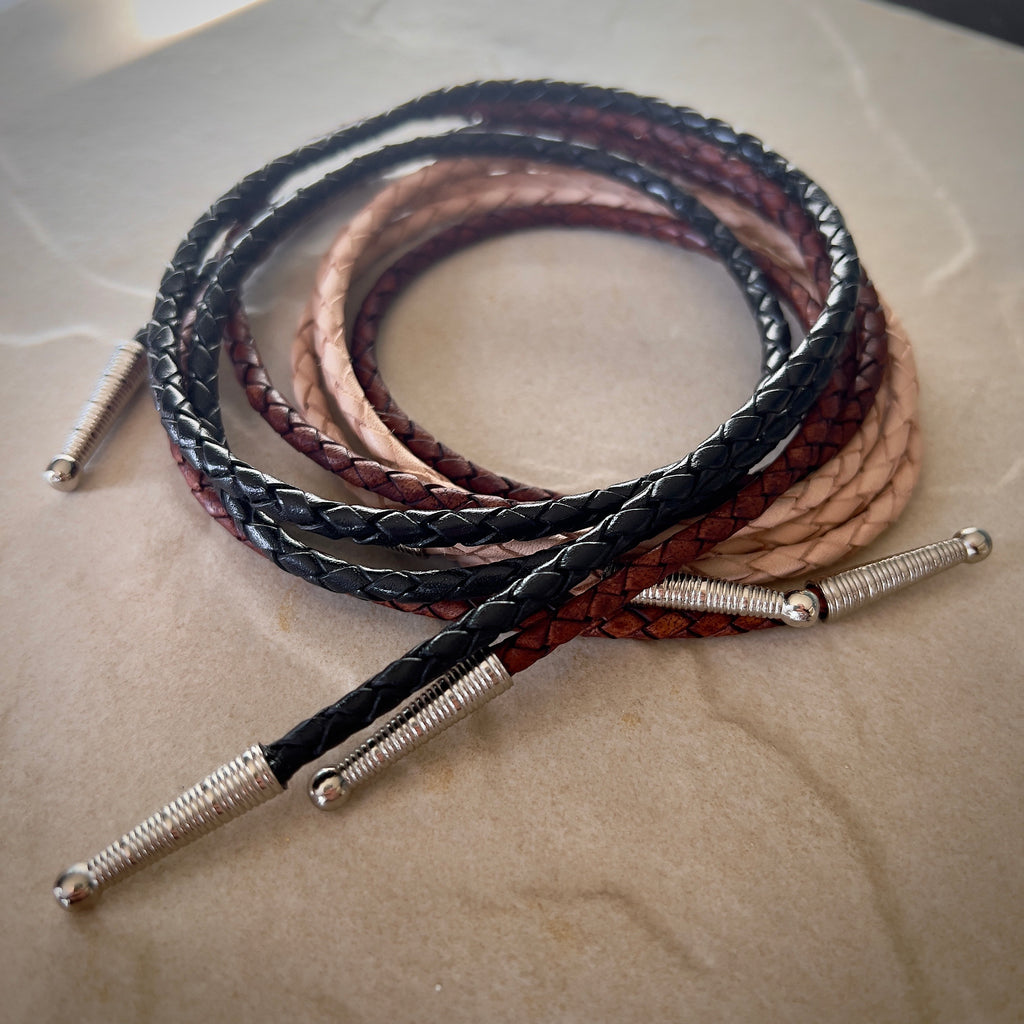 Braided leather cords in black, brown, and beige with silver caps on a light surface.