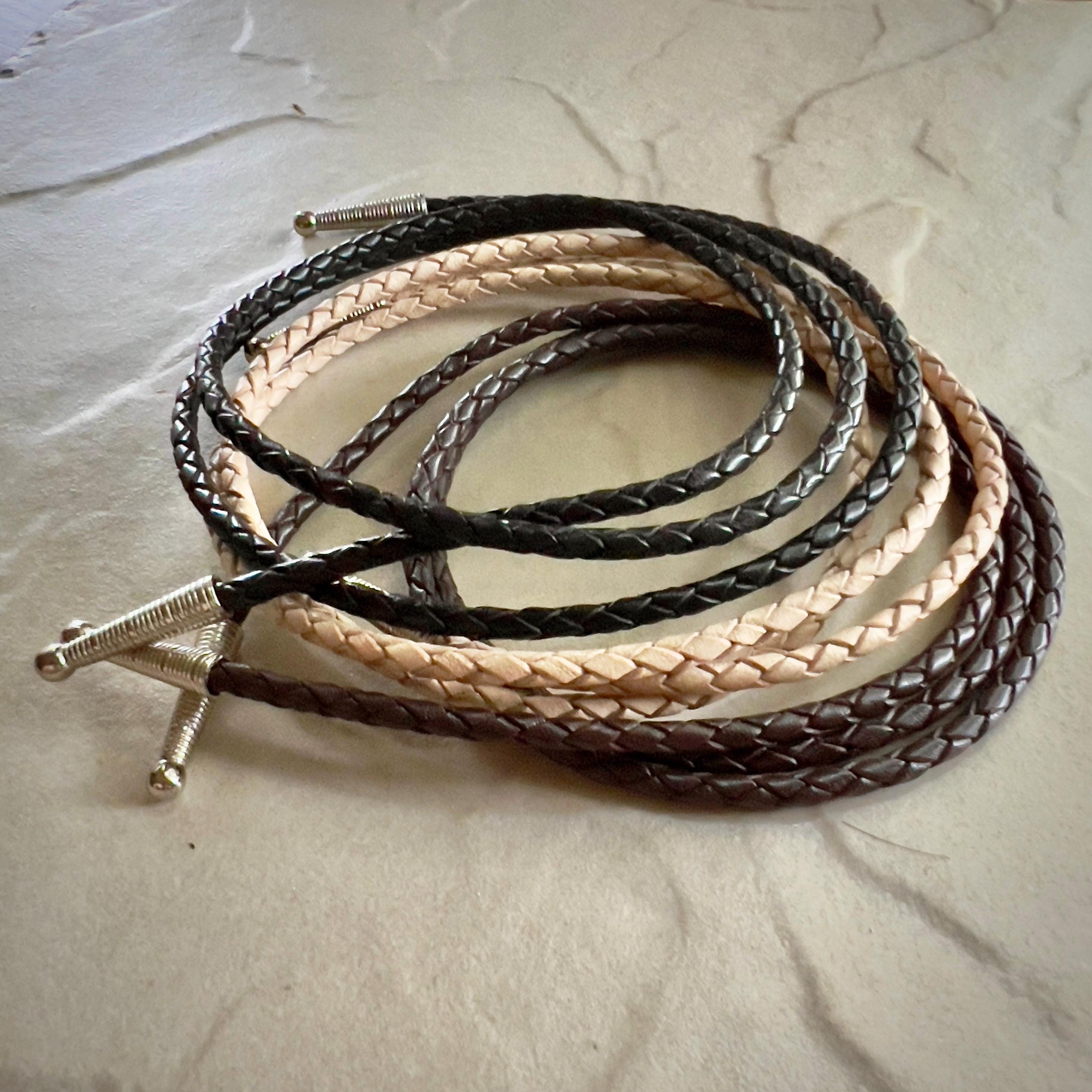 Coiled black, natural and brown  braided leather rope with silver tips on a textured beige surface.