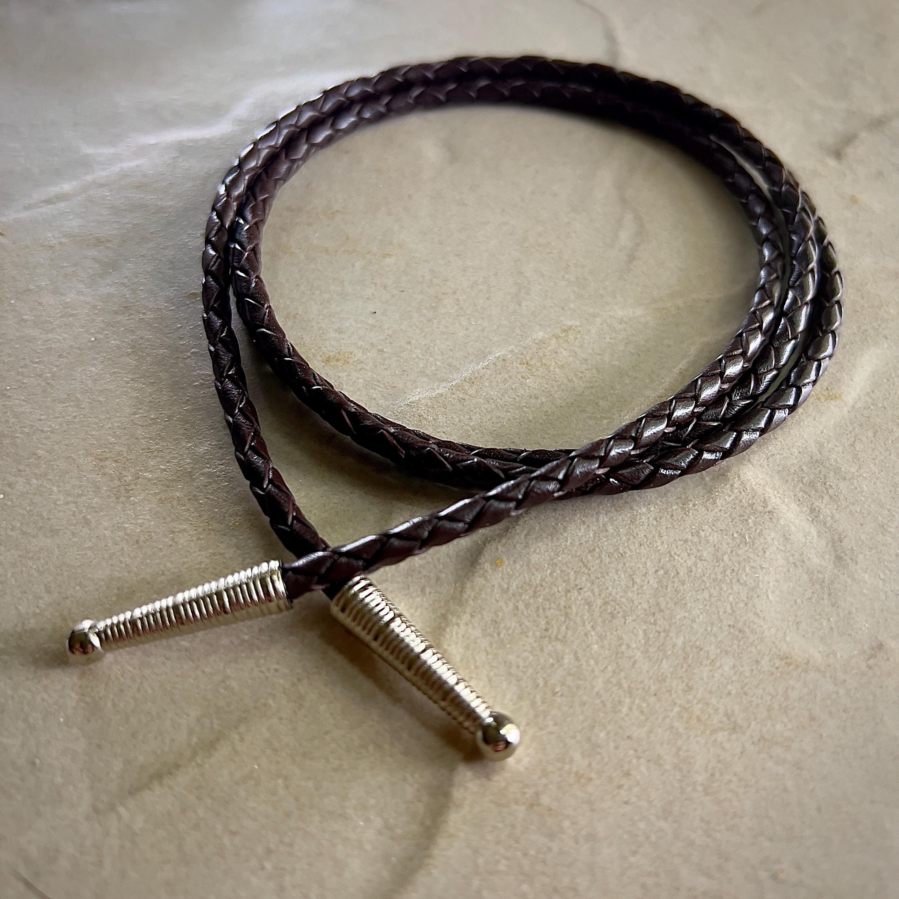 Coiled dark brown braided rope with silver tips on a textured beige surface.