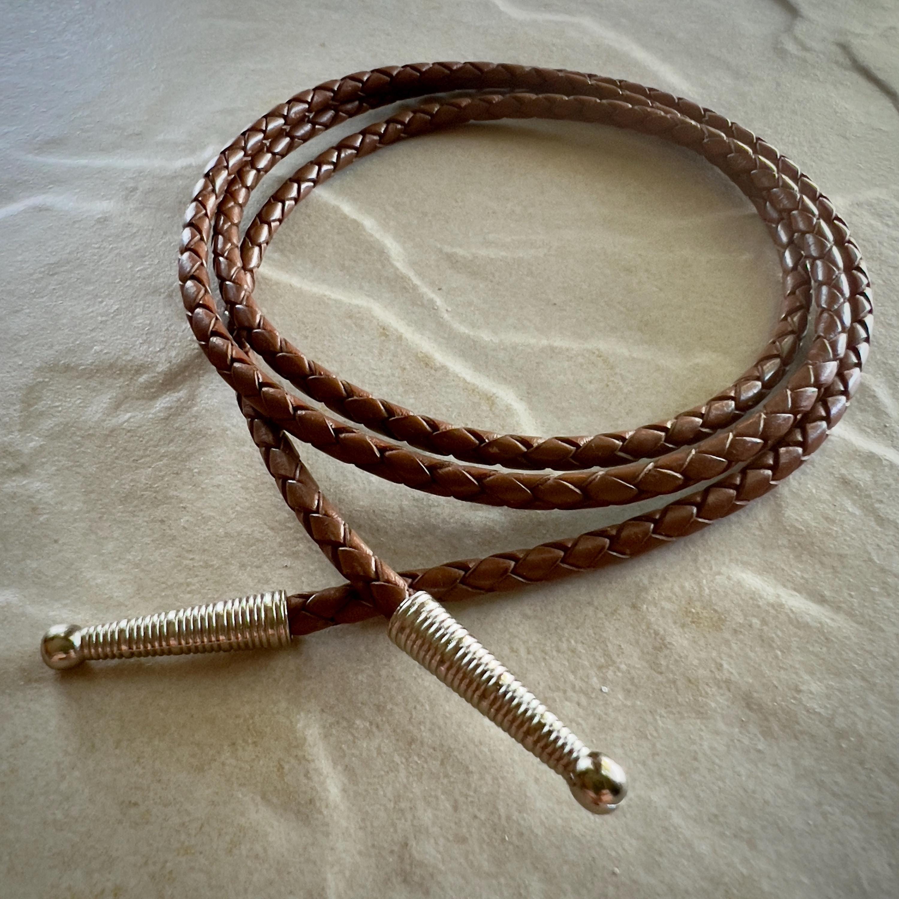 Coiled saddle colored braided rope with silver tips on a textured beige surface.