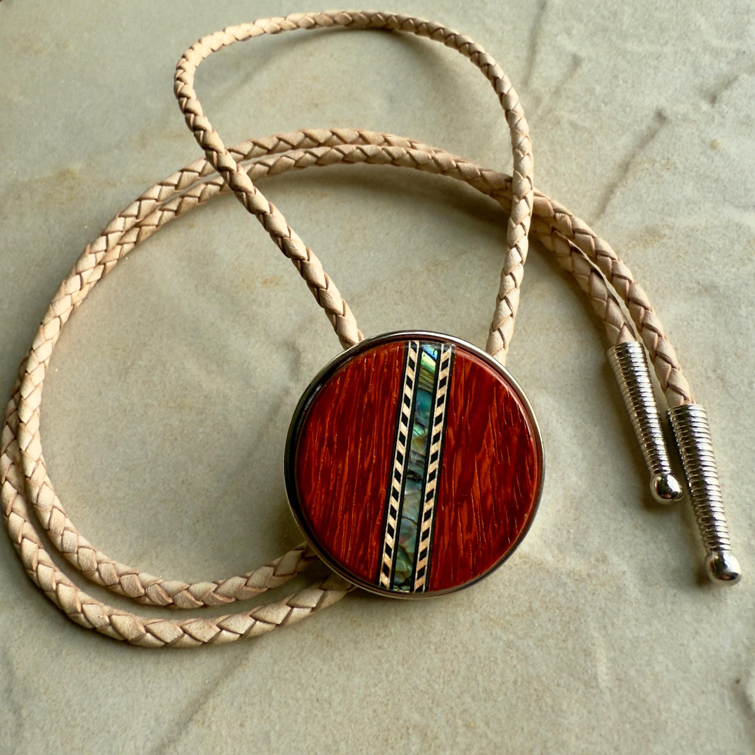 A natural braided leather bolo tie with a round, red wood center with silver tips on a stone background.