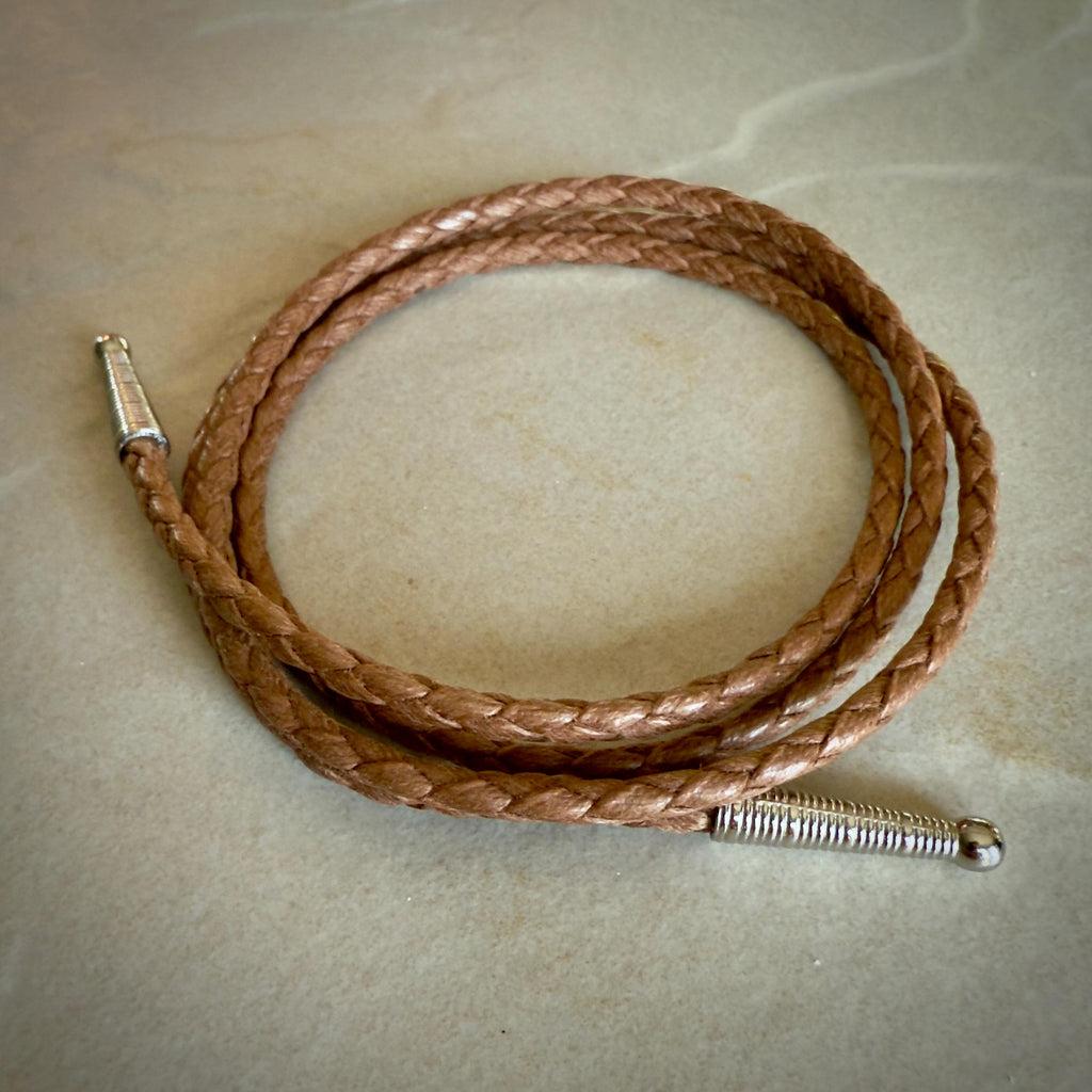Coiled saddle colored braided rope with silver tips on a textured beige surface.
