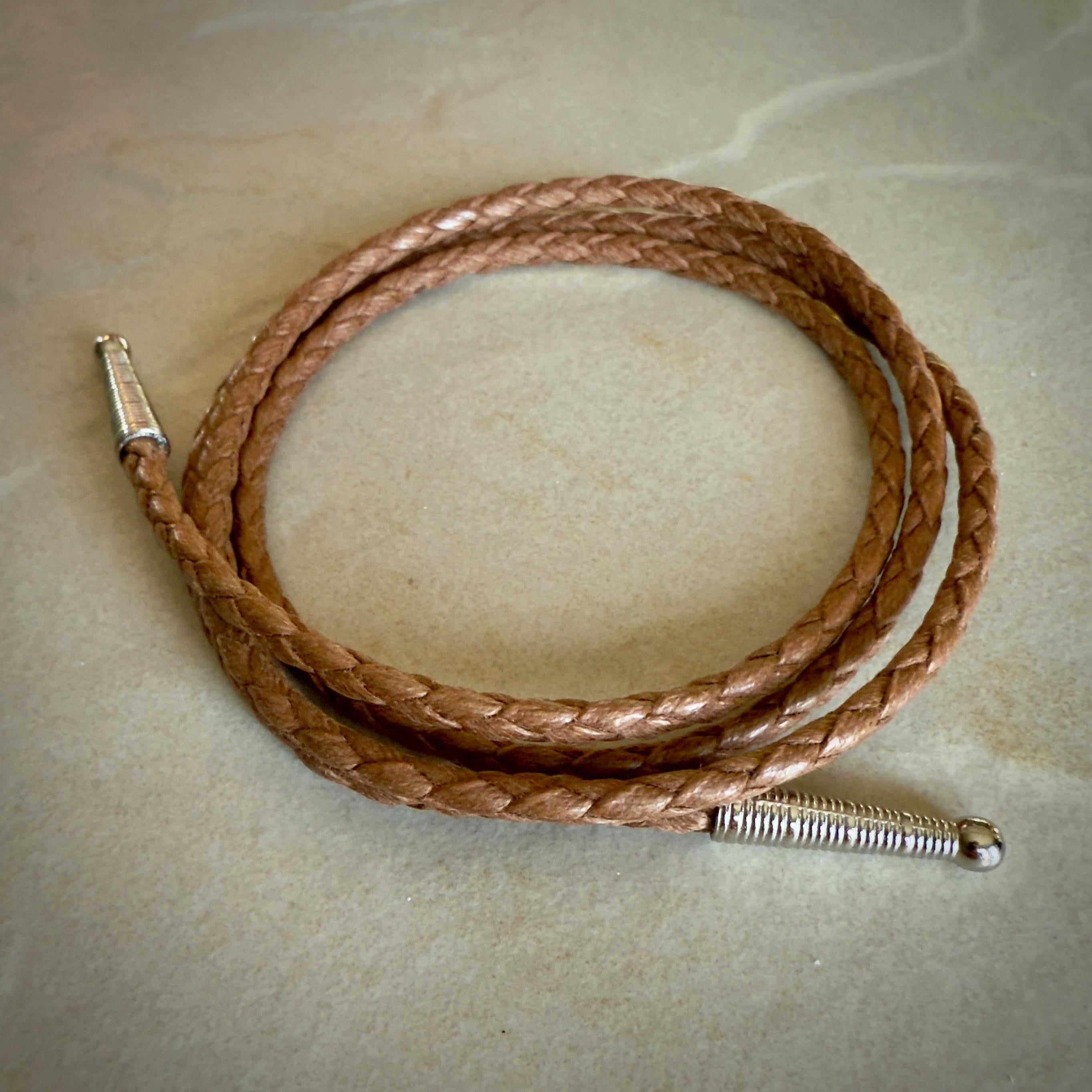 Coiled saddle colored braided rope with silver tips on a textured beige surface.