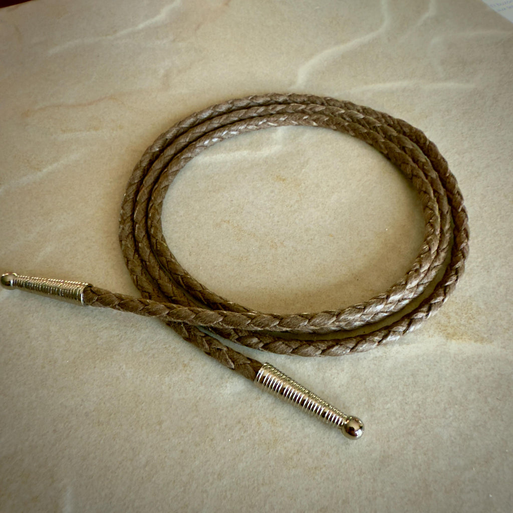 Coiled coffee colored braided rope with silver tips on a textured beige surface.