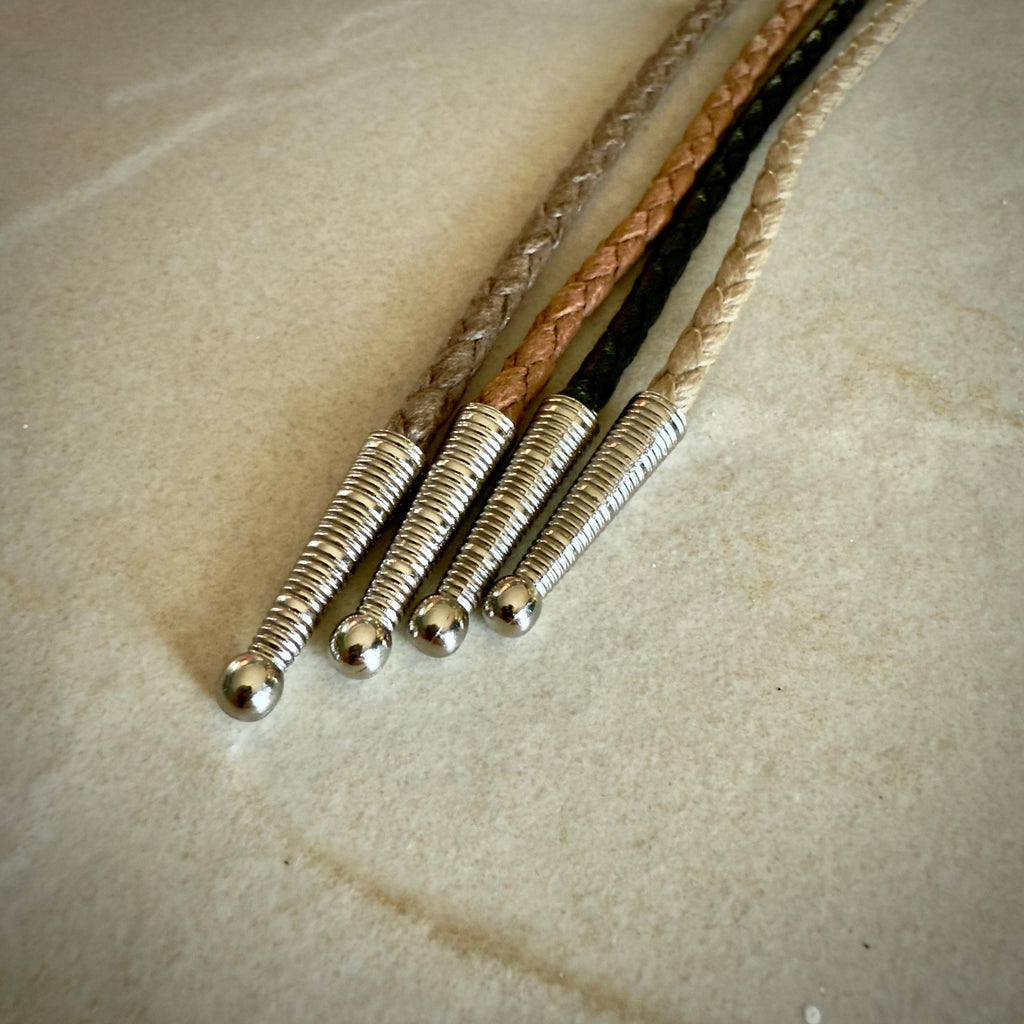 Four stripes of coffee, saddle, black and sand braided leather rope with silver tips on a textured beige surface.