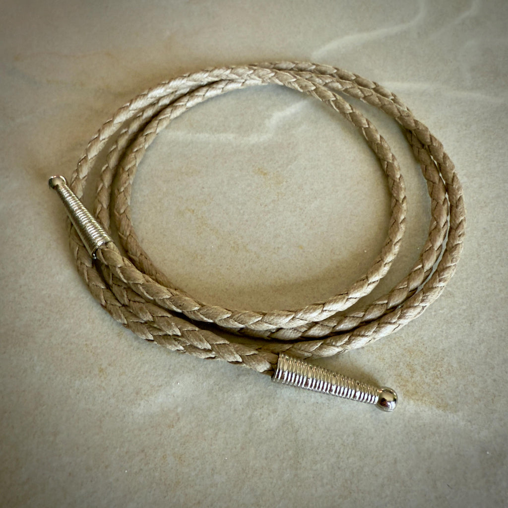 Coiled sand colored braided rope with silver tips on a textured beige surface.