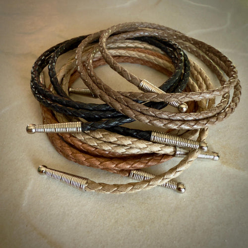Coiled coffee, black, sand and saddle braided cotton rope with silver tips on a textured beige surface.