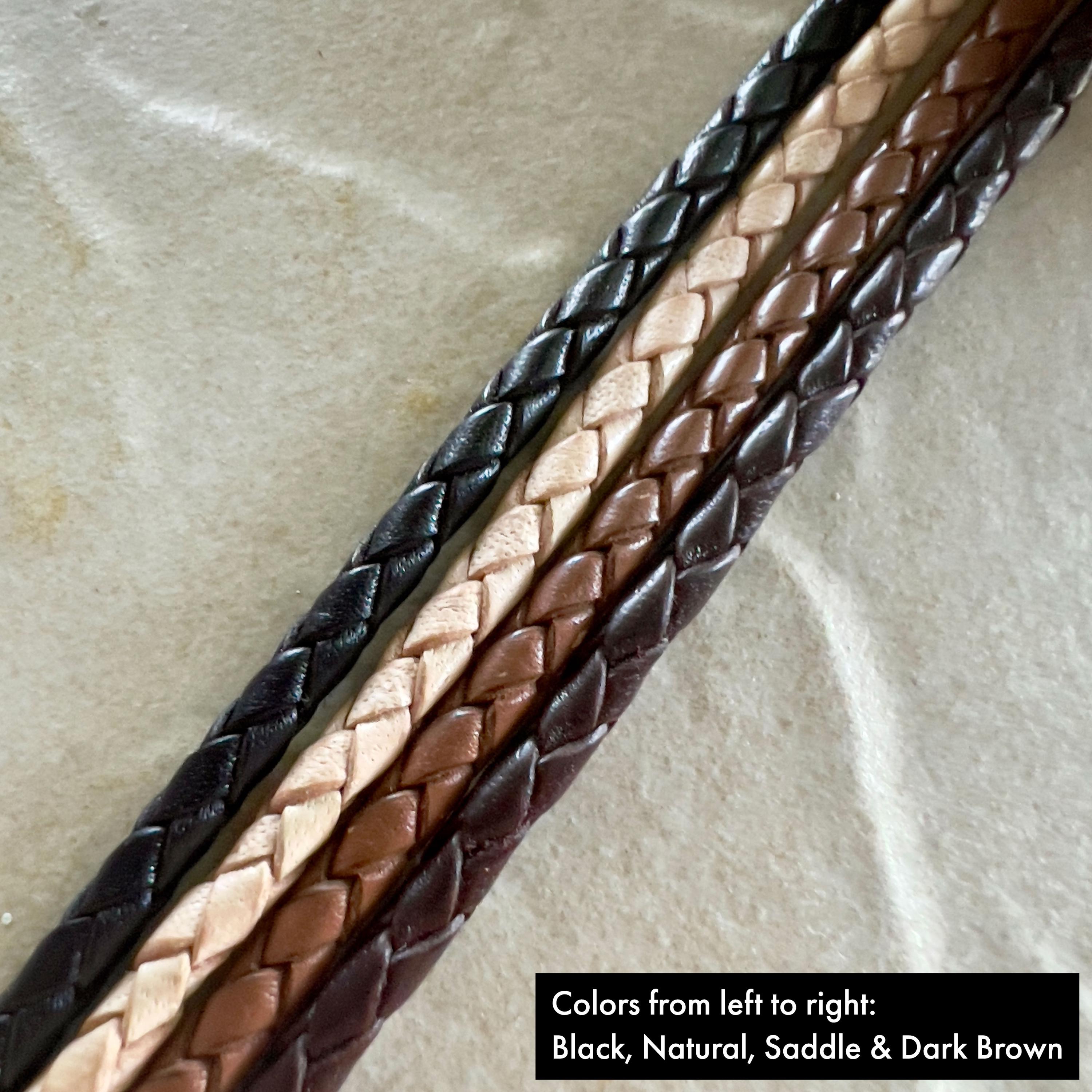 Four stripes of black, natural, saddle and brown braided leather rope on a textured beige surface.